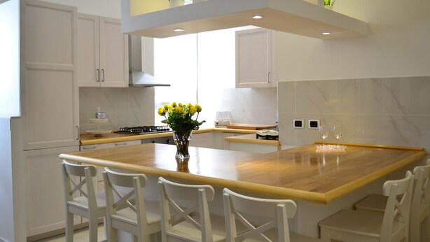 A modern kitchen with white cabinetry, a wooden island, and a vase of yellow flowers. - Ursa Major - Gioligio Rome Central Luxury Suite (Rome)