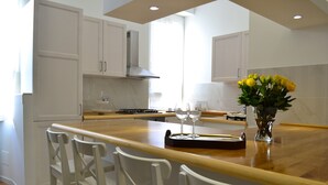 A modern kitchen with white cabinets, a wooden island with bar stools, and a vase of yellow flowers. - Ursa Major - Gioligio Rome Central Luxury Suite (Rome)