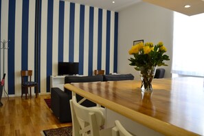 Una sala moderna con una mesa de comedor de madera, un conjunto de sofás, un televisor y un jarrón con flores amarillas.
