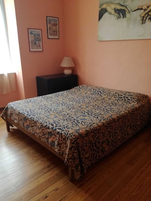 A bedroom with a patterned bedspread, a nightstand with a lamp, and two framed pictures on the wall.