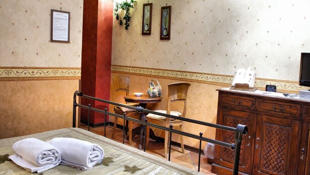A hotel room with a bed, a desk, a chair, a wooden cabinet, and a wall with framed pictures and a certificate. - Dependance Naples City Centre (Naples)