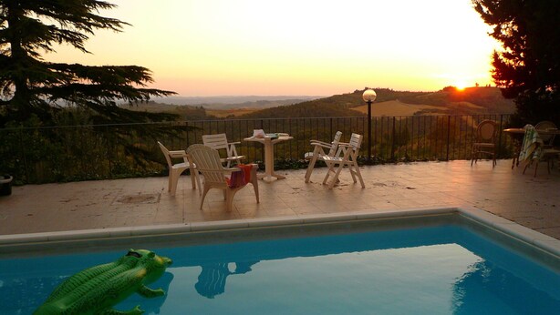 A swimming pool with a green inflatable crocodile, surrounded by outdoor furniture and a scenic view of hills during sunset. - Villa Firenze Casa Serena (Montespertoli)