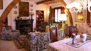 A cozy living room with a fireplace, floral-patterned furniture, and a chandelier. - Villa Firenze Casa Serena (Montespertoli)