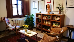 A cozy living room with a wooden bookshelf, a floral armchair, a wicker sofa, and a table with a vase of flowers. - Villa Firenze Casa Serena (Montespertoli)