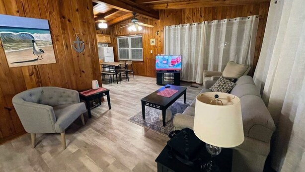 A cozy living room with wooden walls, a television, a sofa, a chair, and a coffee table.