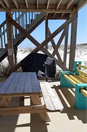 A wooden deck with a picnic table and benches, overlooking a sandy beach with dunes in the background.