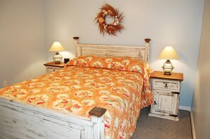 A bedroom with a bed, two bedside tables, a nightstand, a wall-mounted lamp, and a decorative wreath.