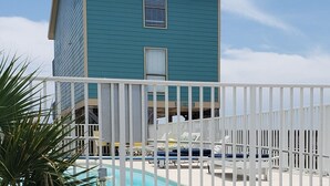 Un bâtiment à deux étages avec une piscine à l’avant, agrémenté d’une clôture blanche et de chaises longues.
