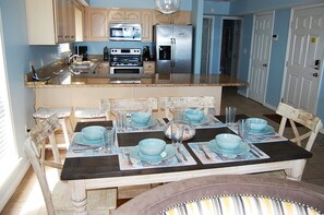 A kitchen with wooden cabinets, a stainless steel refrigerator, and a dining table set with blue bowls and plates.