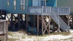 Une maison à deux étages située en bord de mer, dotée d’un balcon à l’étage supérieur, d’une terrasse en bois et d’un escalier menant à l’entrée.