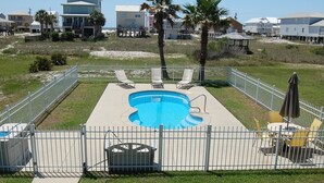 A swimming pool with a deck, surrounded by a white fence, and palm trees in the background.