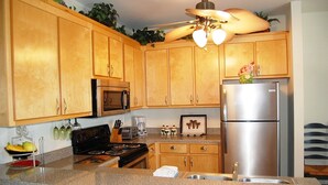 A kitchen with wooden cabinets, a stainless steel refrigerator, a microwave, a stove, and a ceiling fan.