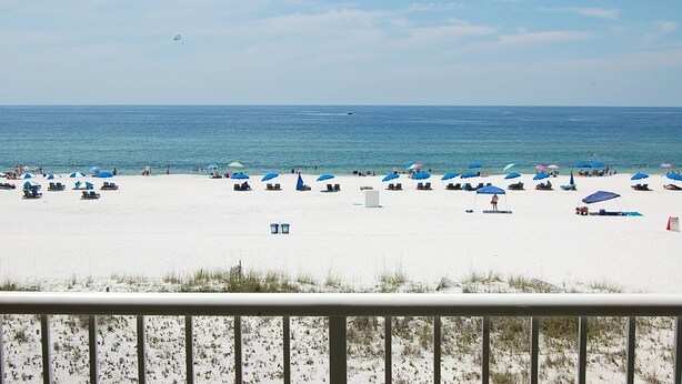 A beach with numerous umbrellas and lounge chairs, a clear sky, and a calm sea.