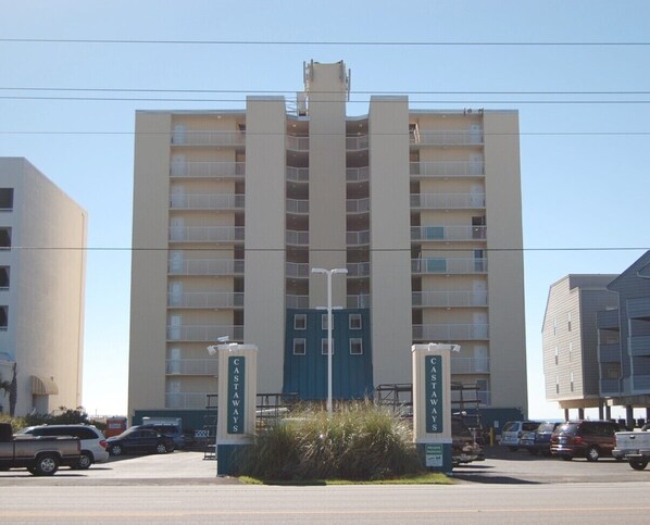 Un hotel de varios pisos con una entrada central, balcones en cada planta y un estacionamiento al frente.