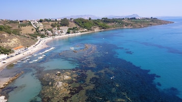 Vista aérea de una zona costera con aguas azules cristalinas, formaciones rocosas y una playa con barcos.
