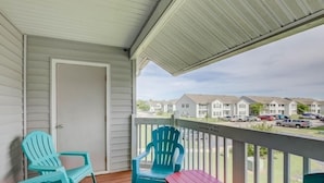 A balcony with two turquoise chairs and a red table, overlooking a row of townhouses.