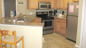 A kitchen with wooden cabinets, a stainless steel refrigerator, a microwave, a stove, and a sink. - 2BR Gulf Shores Condo | Central Location + Short Drive to Beach (Gulf Shores)