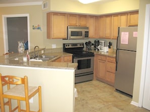 A kitchen with wooden cabinets, a stainless steel refrigerator, a microwave, a stove, and a sink. - 2BR Gulf Shores Condo | Central Location + Short Drive to Beach (Gulf Shores)
