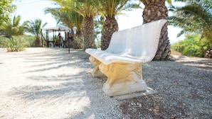 A bench with intricate carvings, set on a gravel path surrounded by palm trees. - Studio 200 Meters From the Sea, Wifi, Self Catering (Sciacca)