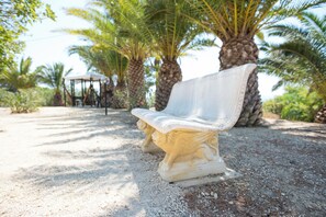A bench with intricate carvings, set on a gravel path surrounded by palm trees.