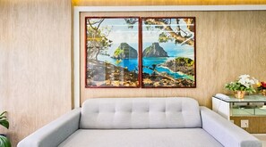 Une pièce avec un canapé gris, un mur en bois et un grand tableau encadré représentant un paysage côtier.