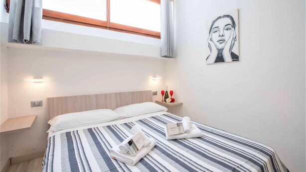 Una habitación de hotel con cama, mesita de noche, un cuadro en la pared y ventana con cortinas.