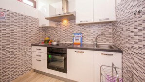 Una cocina compacta con armarios blancos, una campana extractora de acero inoxidable, horno empotrado y salpicadero de azulejos.