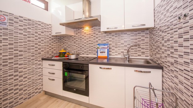 Una cocina compacta con armarios blancos, una campana extractora de acero inoxidable, horno empotrado y salpicadero de azulejos.