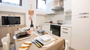 Una cocina moderna con armarios blancos, horno empotrado y comedor con mesa para dos.
