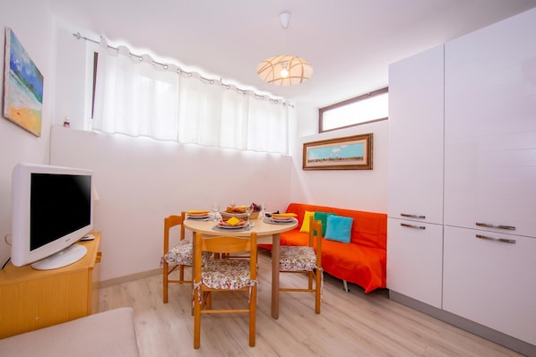 A dining area with a table, chairs, a television, a sofa, and a cabinet.