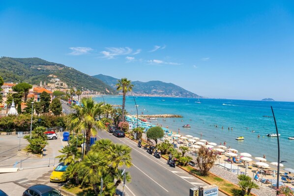 Una carretera costera con coches estacionados, palmeras y sombrillas de playa.