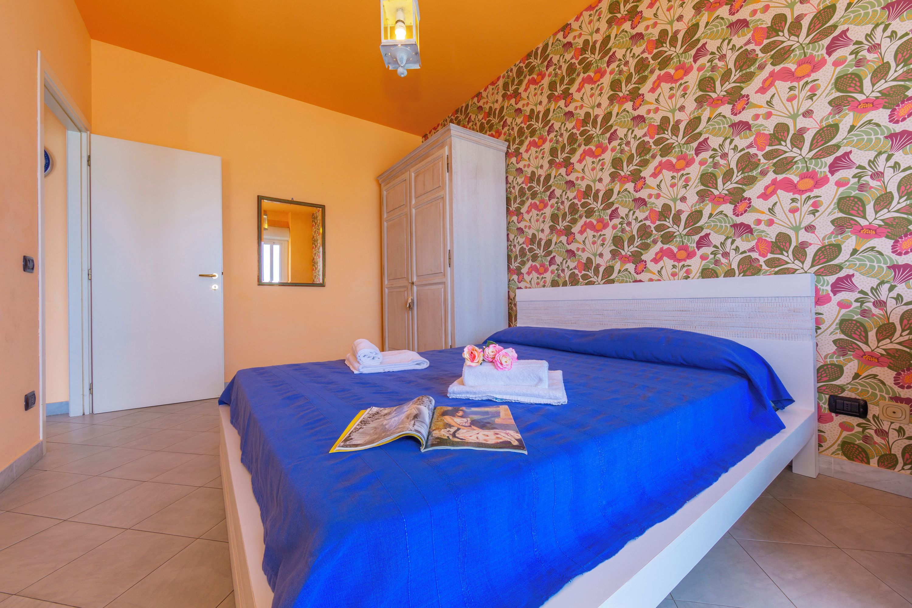 Ein Schlafzimmer mit einem Bett, einem Kleiderschrank, einem Spiegel und blumigem Wandpapier.
