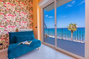 A room with a teal sofa, a patterned wall, and a balcony with a view of the sea. - Laigueglia Beach (Laigueglia)