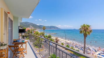 Un balcon donnant sur une plage, une table avec des chaises et un téléviseur fixé au mur.