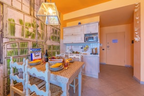 A kitchen with a dining table set for two, a microwave, and a window with cactus decoration.