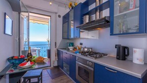 A modern kitchen with blue cabinets, stainless steel appliances, and a view of the sea through an open door. - La Casa Al Sole Sea View 400mt From Sea (Andora)