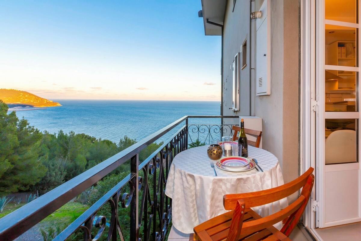 A balcony with a table set for two, overlooking a body of water and greenery.