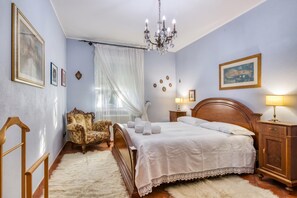 A bedroom with a wooden bed, a chair, a nightstand with a lamp, and a chandelier. - La Casetta Sull'Albero child friendly (Albenga)