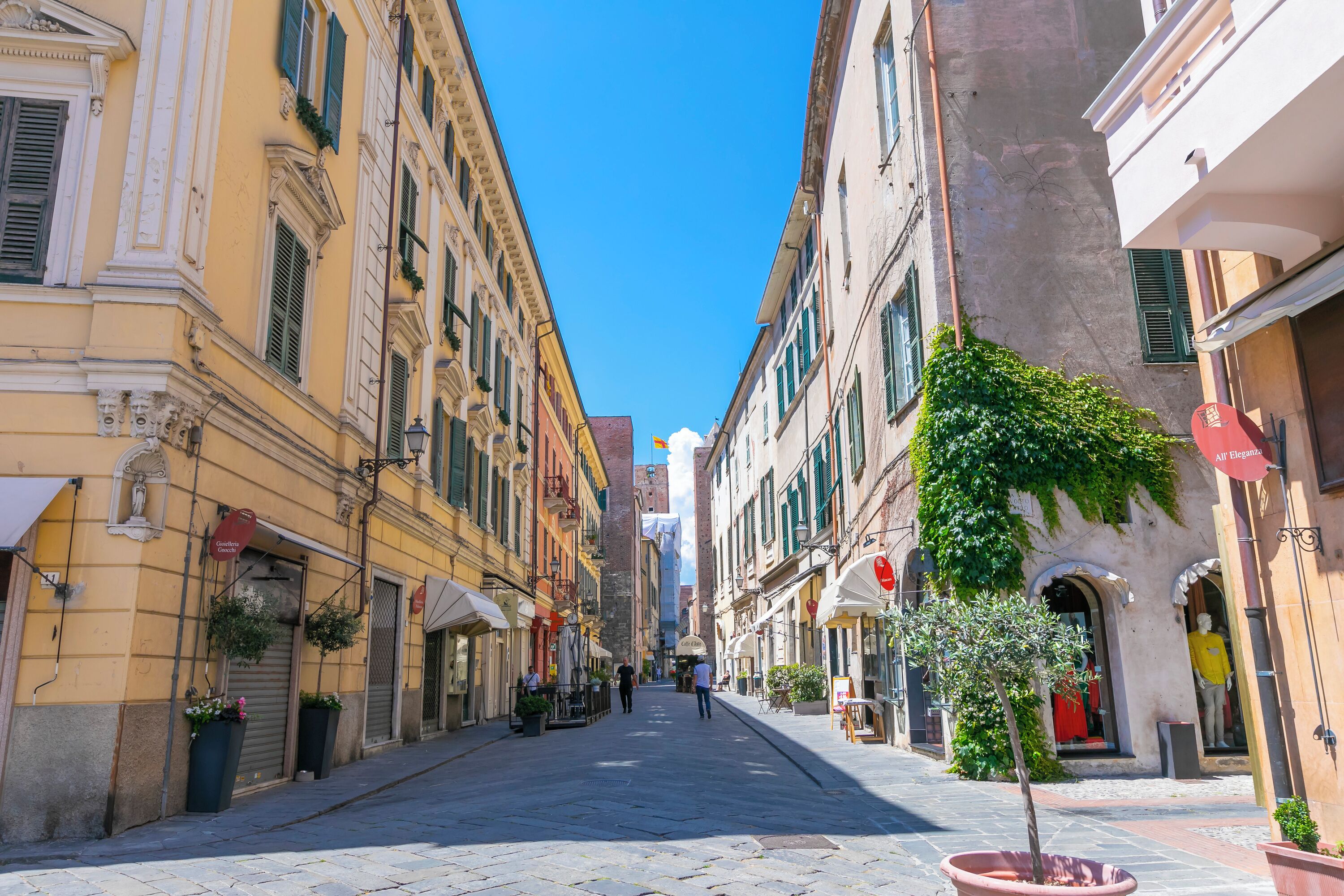 A narrow street lined with historic buildings, some with shutters and potted plants.