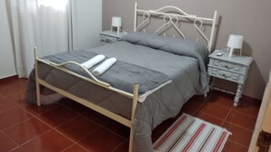 A bedroom with a metal bed frame, grey bedding, a bedside table with a lamp, and a striped rug.