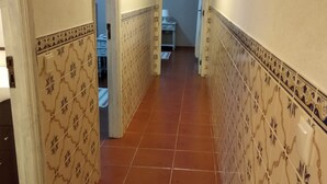 A hallway with patterned walls and a tiled floor, leading to a room with a bed and a nightstand.