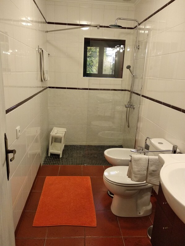 A bathroom with white tiled walls, a shower, a toilet, and a sink.