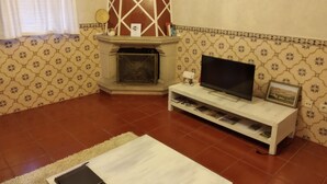 A living room with a fireplace, a television on a stand, and patterned wallpaper.