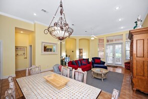 A spacious living room with a chandelier, a dining table, and a large wooden cabinet.