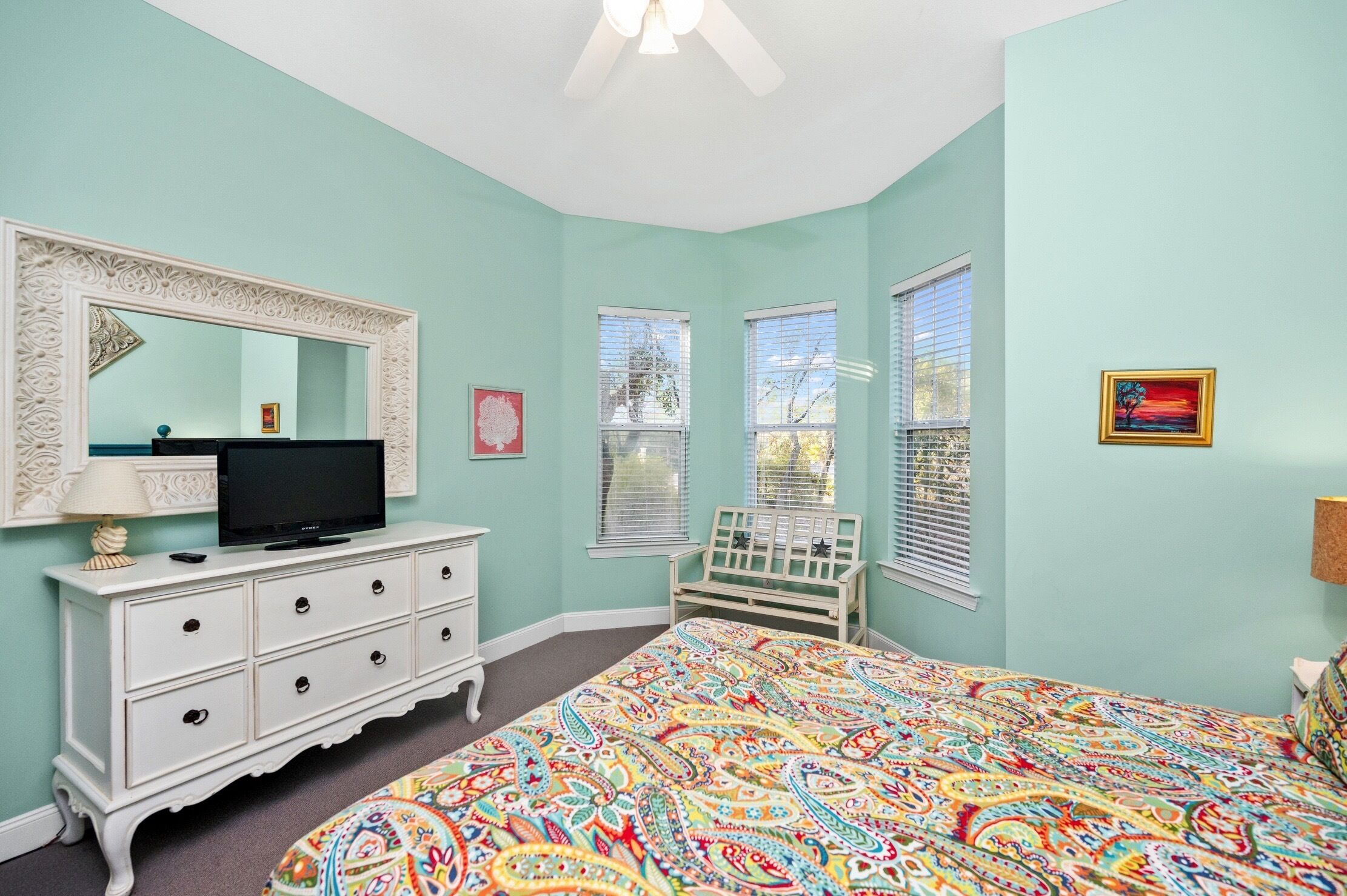 Un dormitorio con cama, cómoda, televisor y ventanas.