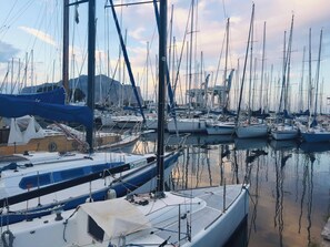 A marina with multiple boats docked, calm water, and a mountainous backdrop.