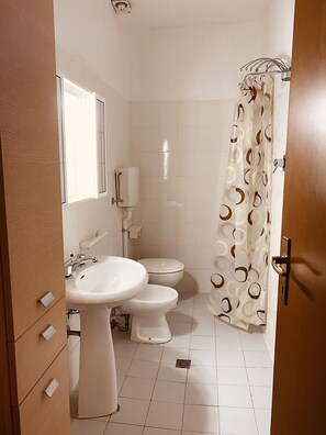A bathroom with a sink, two toilets, a shower curtain, and a window.