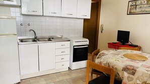 A compact kitchen with white cabinets, a sink, and a stove. There is a dining area with a table and chairs, and a computer on the table.