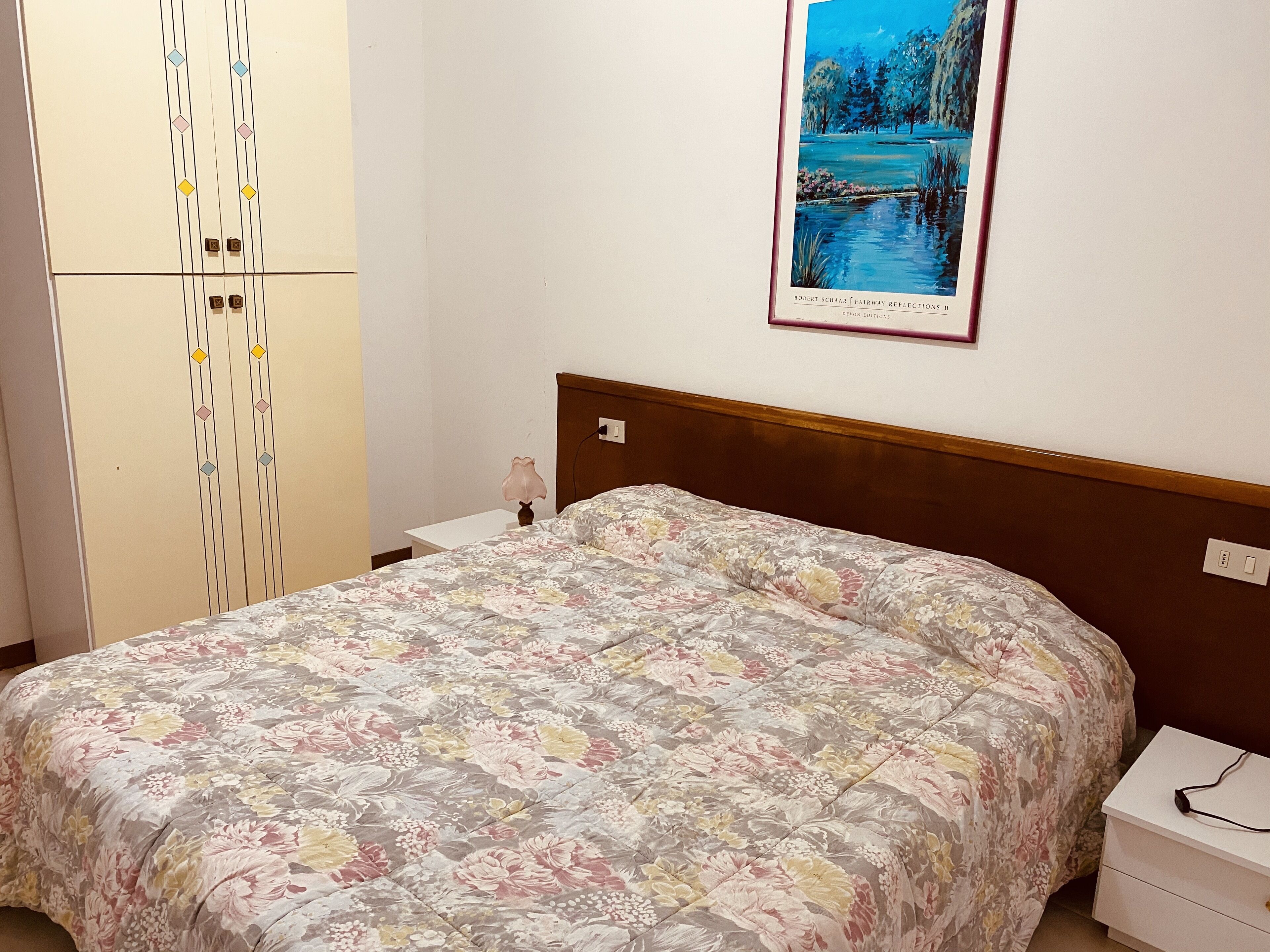 A bedroom with a bed, a nightstand, a wardrobe, and a framed picture on the wall.