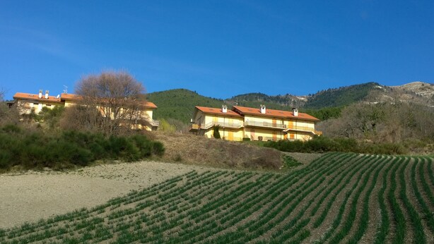 A two-story building with a red roof, surrounded by green fields and hills.